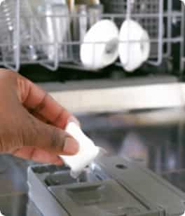 Mano de una persona colocando una tableta de lavavajillas en una máquina lavaplatos gris
